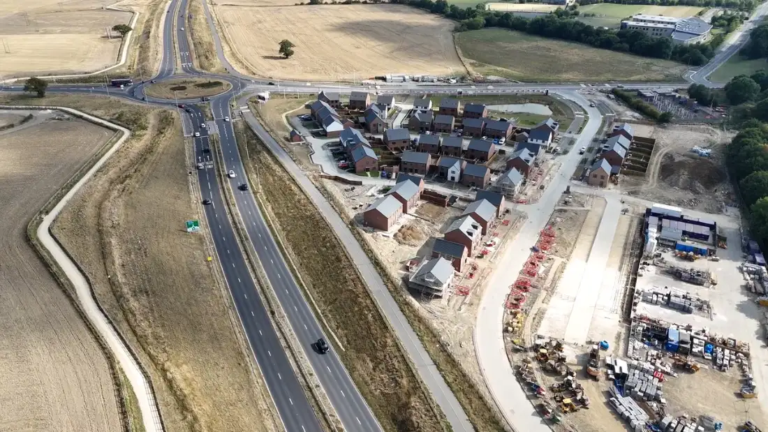 Aerial view of a new dual carriageway and roundabout beside a residential development under construction in England